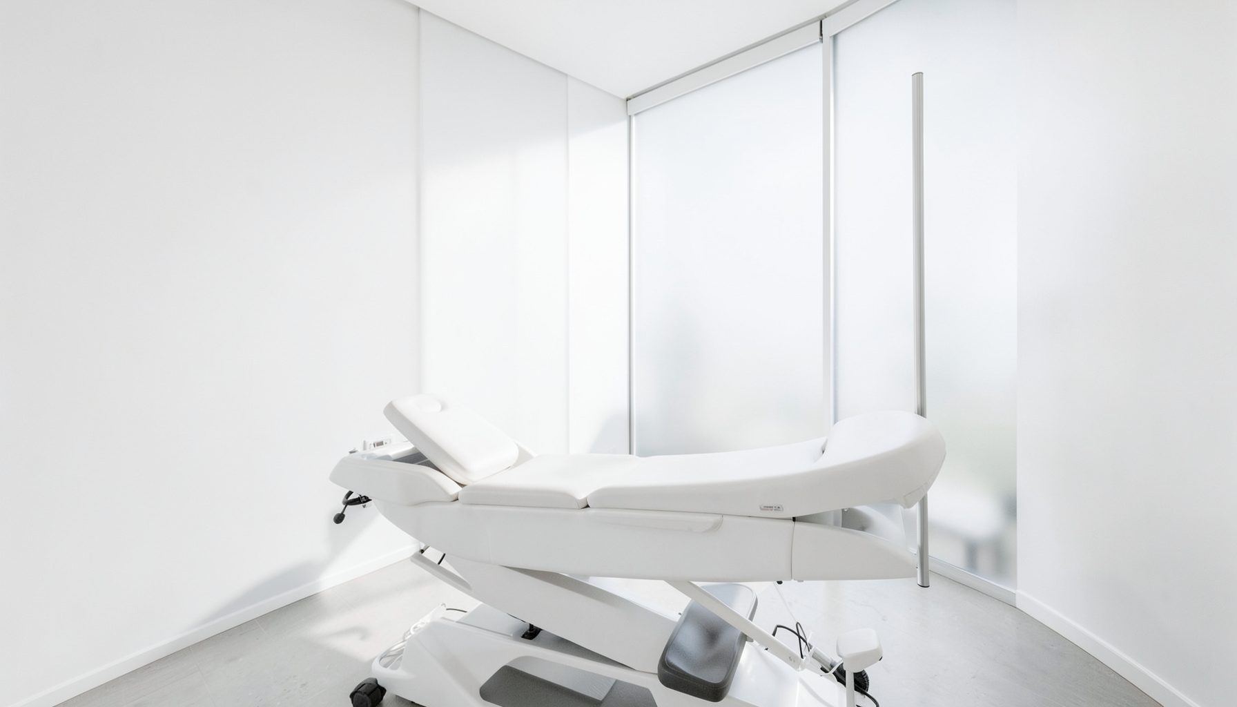A bright, modern aesthetic clinic interior with clean white walls, a sleek treatment bed, and soft natural light streaming through frosted glass