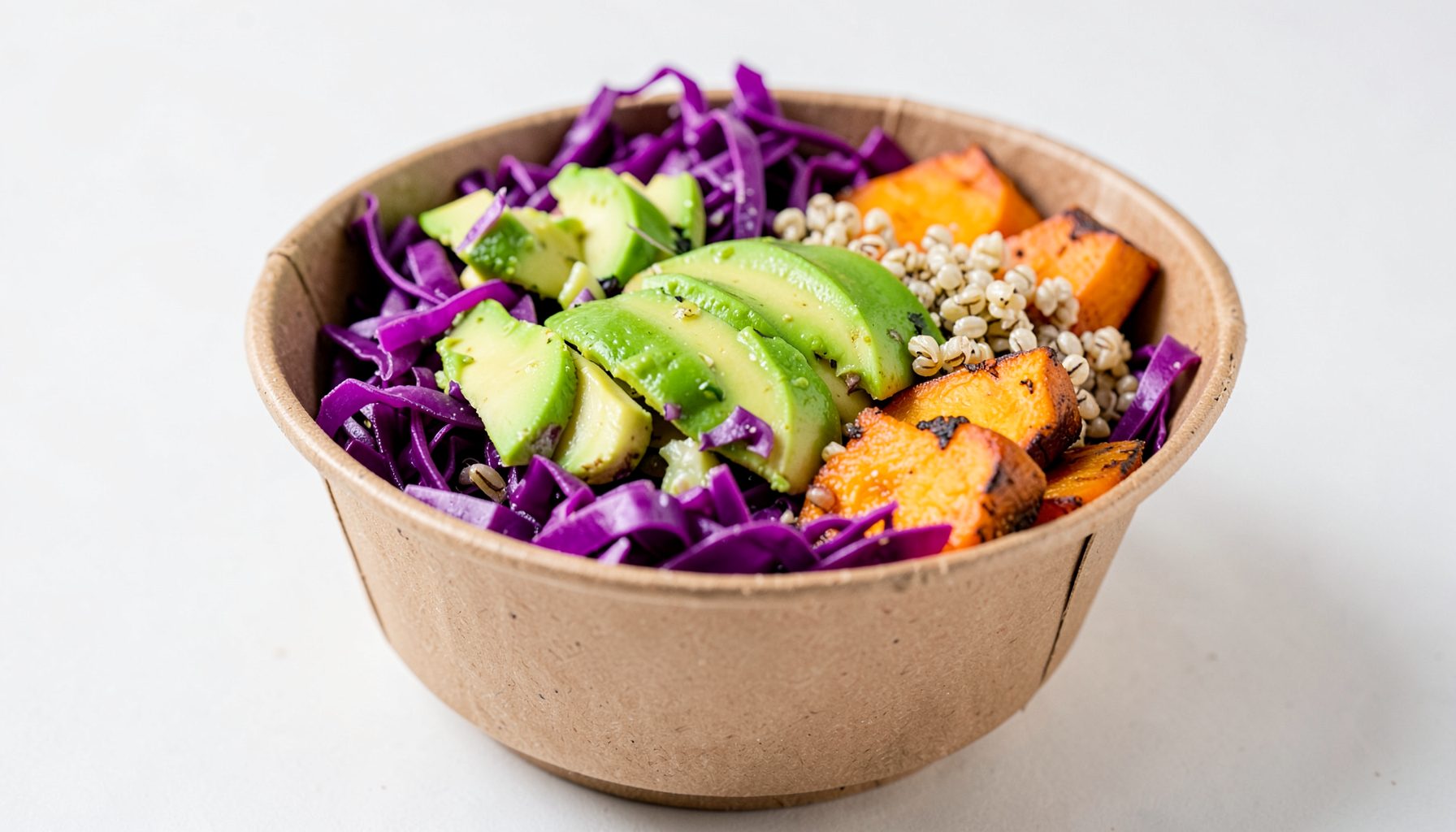 A colorful plant-based superfood bowl in a compostable container, layered with vibrant purple cabbage, avocado slices, quinoa, and roasted sweet potato — bright greens, purples, and warm orange tones.