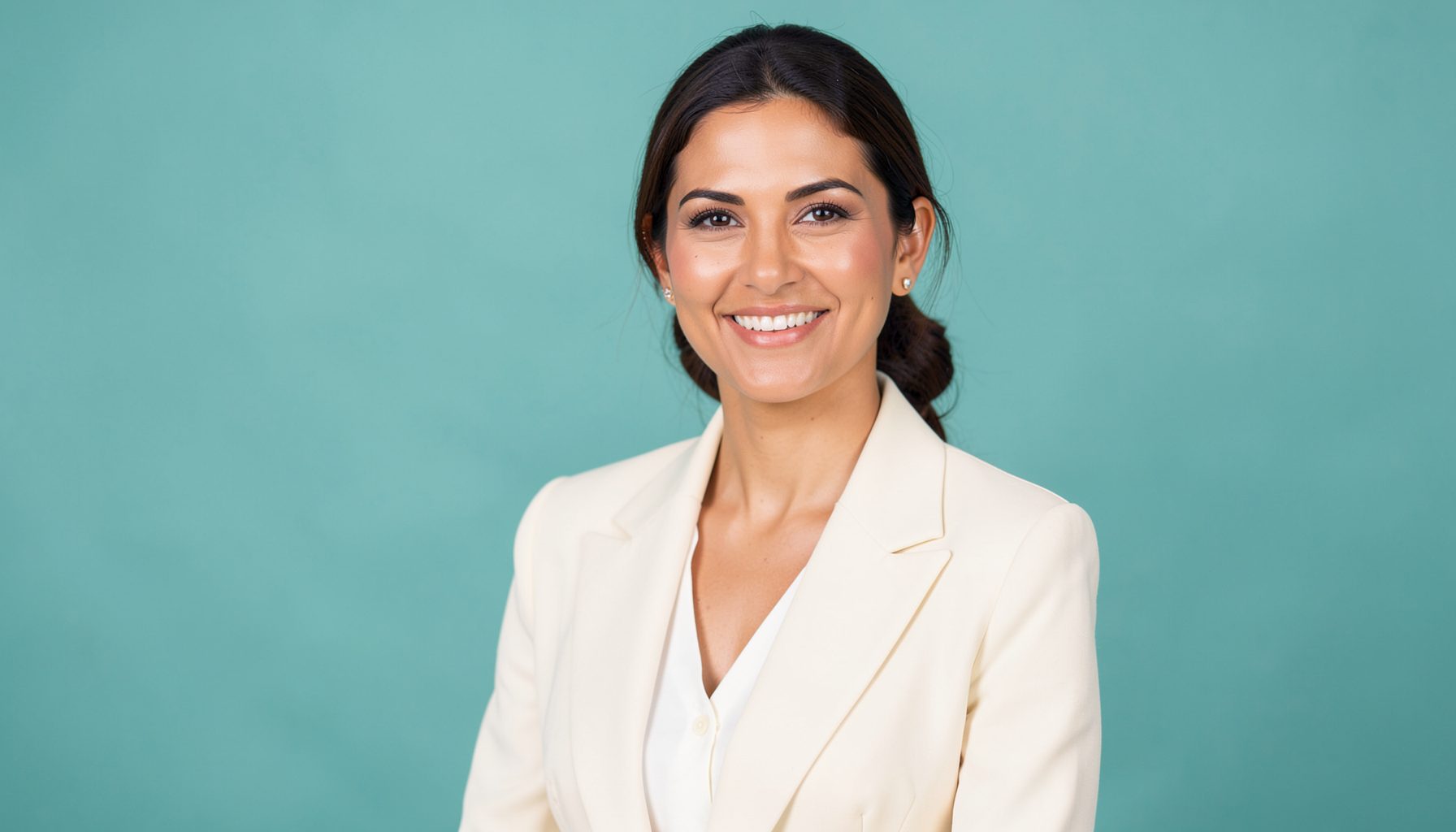 A poised woman in a cream blazer against a soft teal background, exuding warmth and professional confidence.
