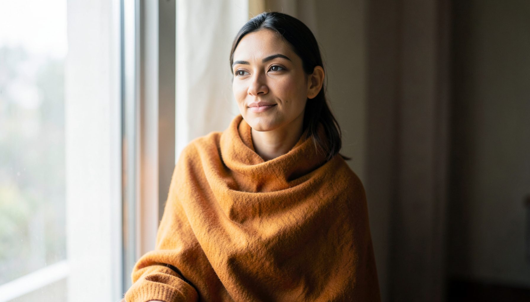 A woman with a serene expression, wrapped in a rich ochre shawl, seated near a window with soft diffused daylight.